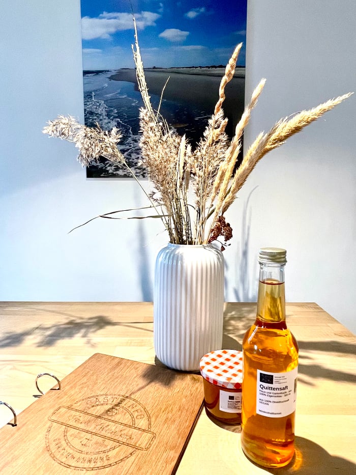 ferienwohnung-amrum-selbstgemachter Saft Selbstgemachter Quittensaft und ein Glas Quittengelee stehen auf dem Tisch neben einer Vase mit trockenen Gräsern.